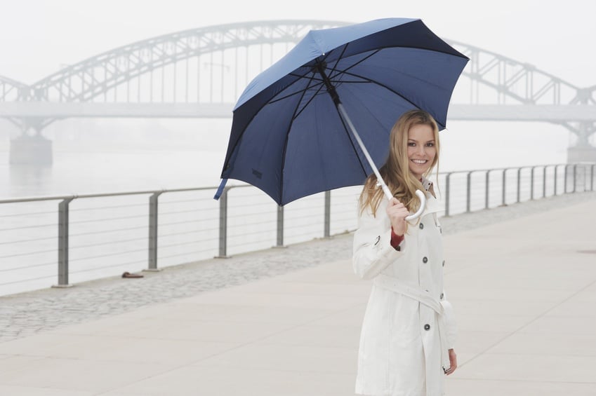 Woman in white coat carrying blue umbrella