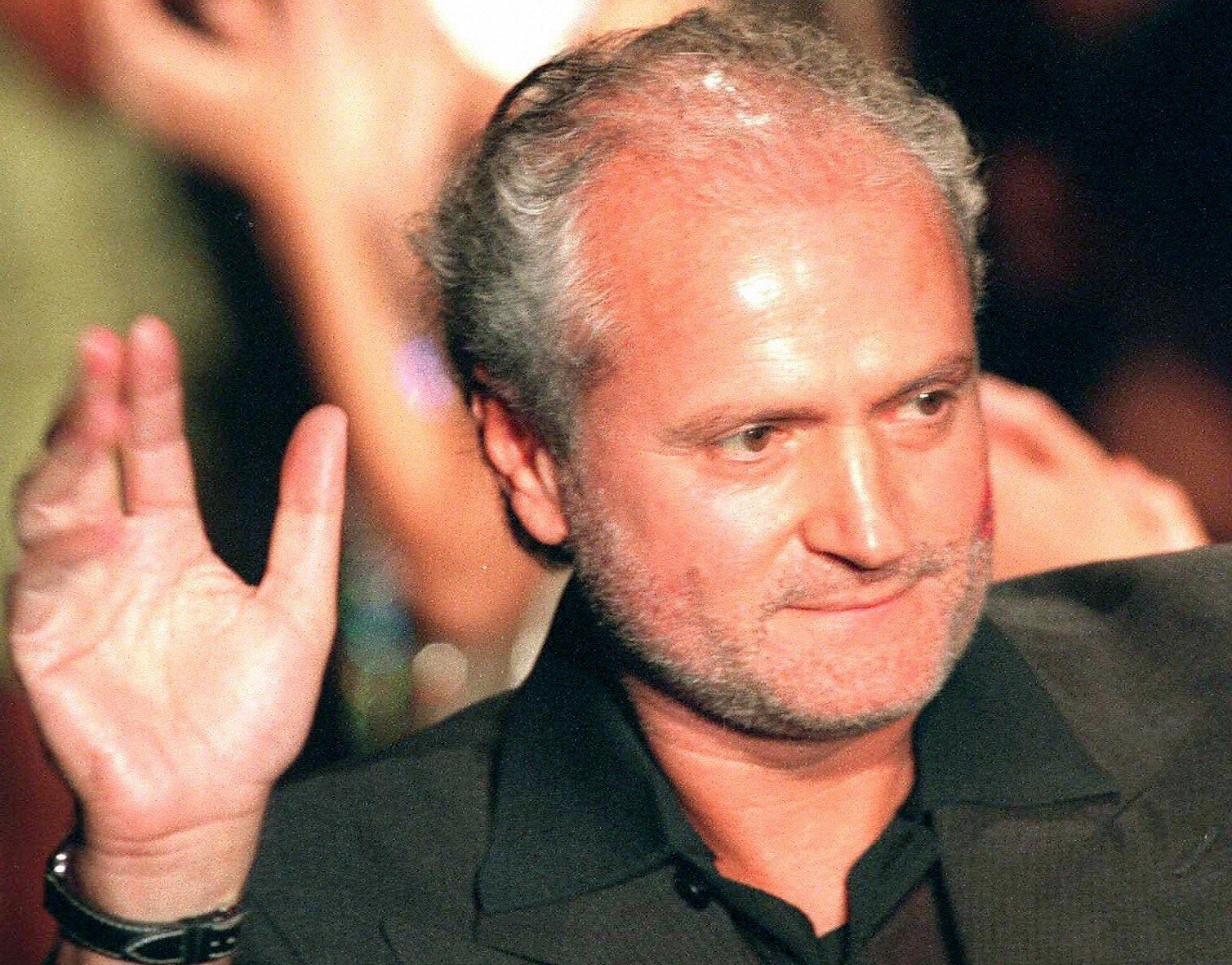 Gianni Versace waving at a crowd during a fashion show. 