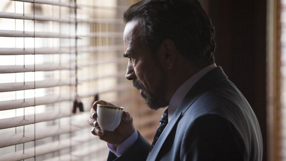 A man holds an espresso in his hand while looking out the window in Narcos Season 2