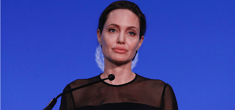 Angelina Jolie wearing a black top, set against a blue UN background.