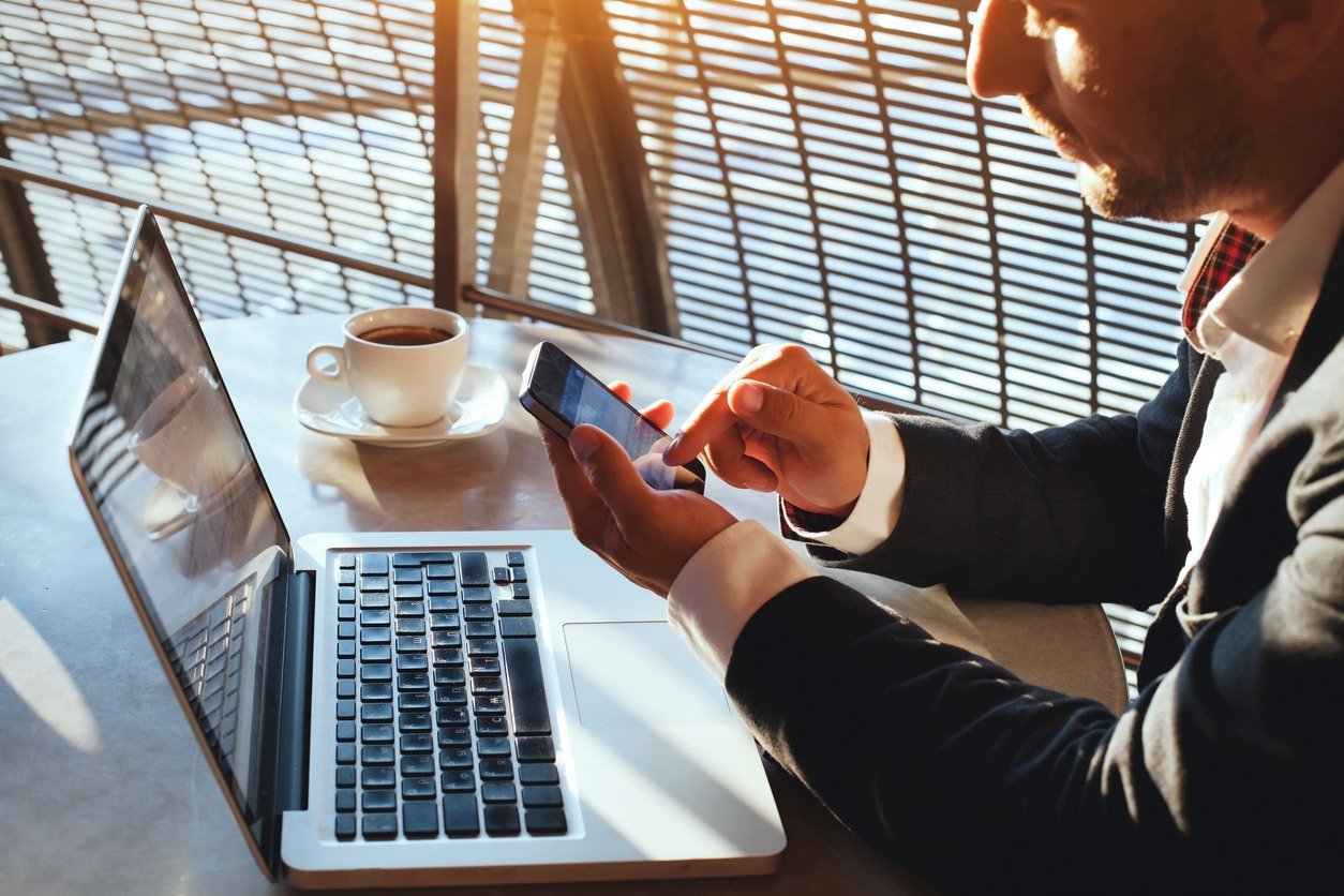 man with computer using phone while sitting outdoors