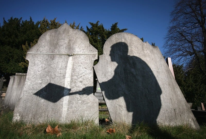 The shadow of a cemetery worker is cast on reclaimed gravestones