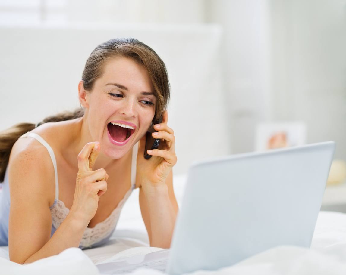 Excited woman with laptop talking on mobile