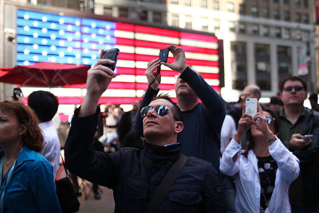 People take pictures as Facebook founder Mark Zuckerberg is viewed on a screen in Times Square