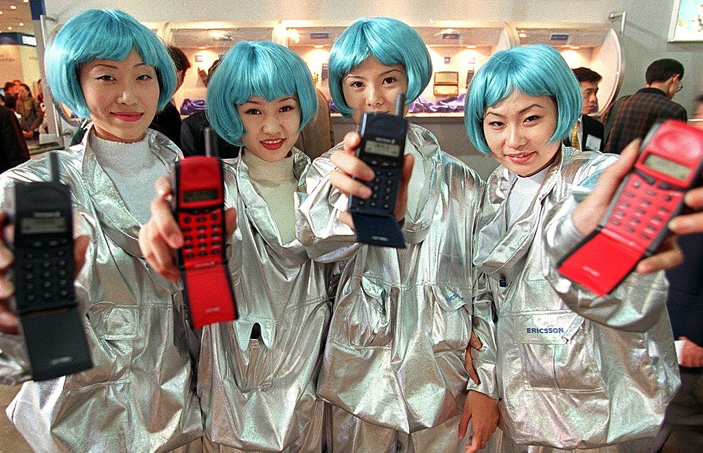 Four Chinese women, wearing blue wigs, display their company's latest mobile phones