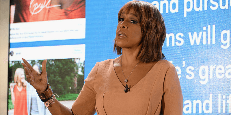 Gayle King standing and waving her hand while at a presentation.
