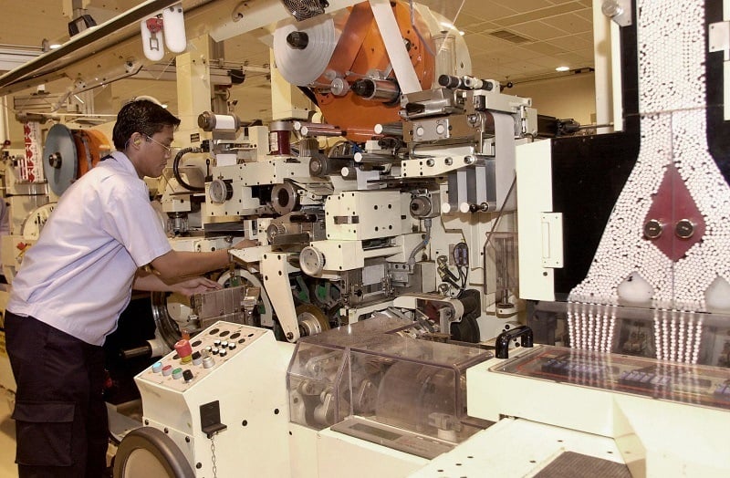 A laborer works at an automated cigarette packaging machine in a Philip Morris tobacco factory