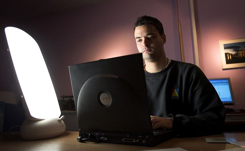 A man suffering from seasonal depression, a common mental health issue, sits in front of a natural light box in his office