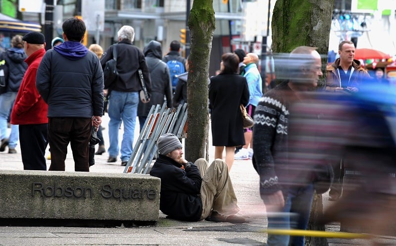 A homeless man sits on the street in downtown Vancouver, emblematic of the city's affordable housing crisis