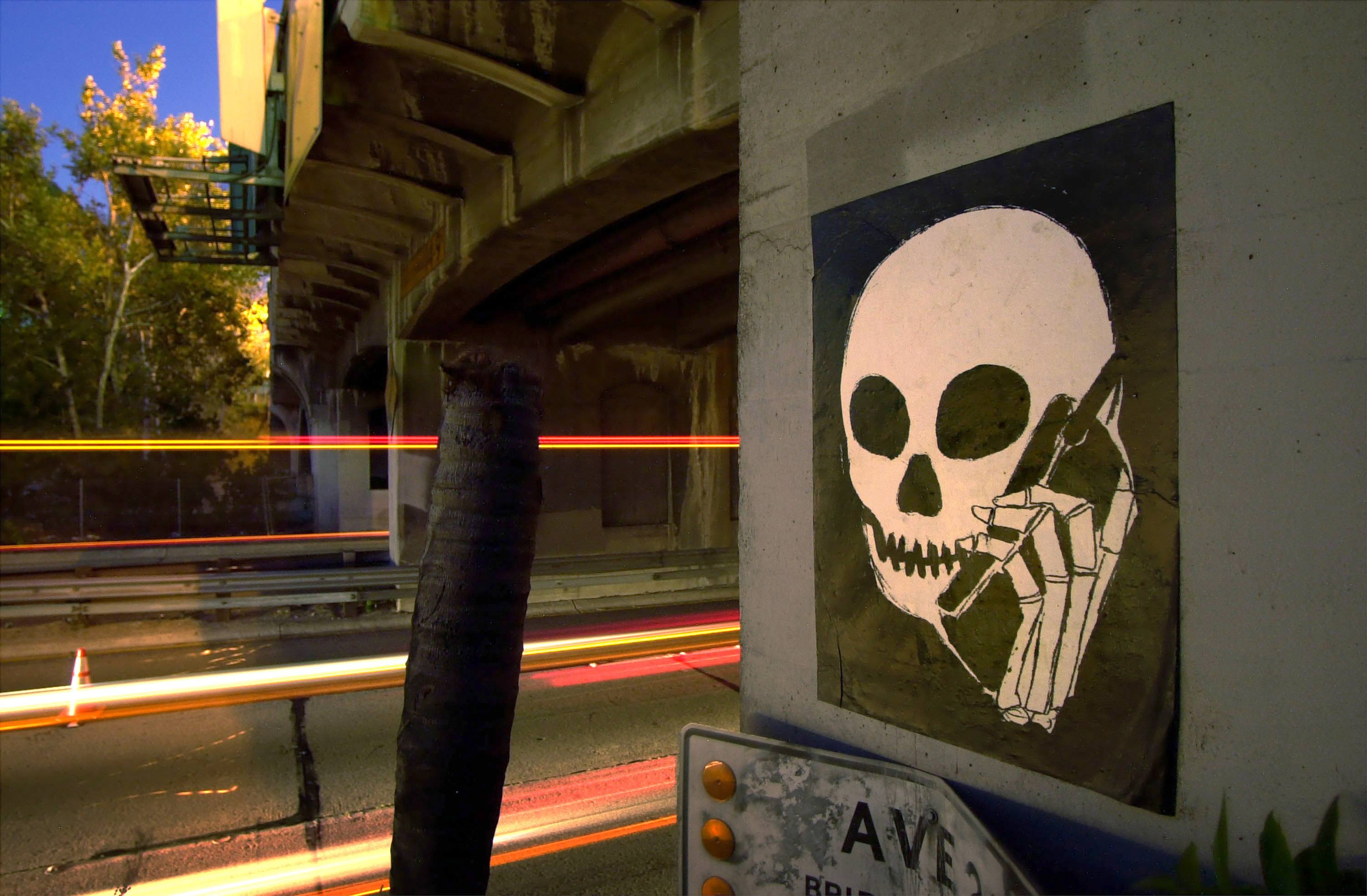 A graffiti image of a skull holding a cell phone is painted on an underpass along the Pasadena Freeway