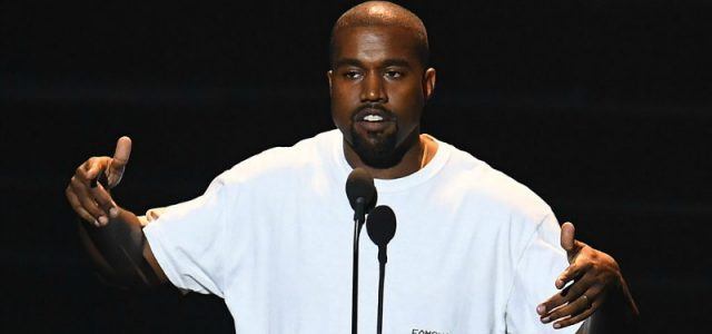 Kanye West in white t-shirt speaking into a microphone.