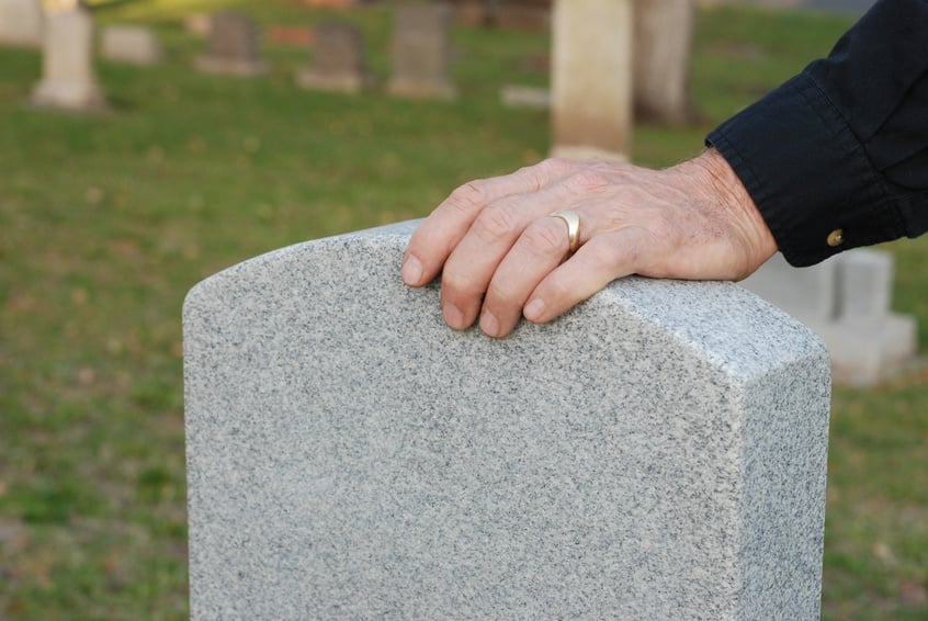 man's hand, with wedding ring, resting on a headstone