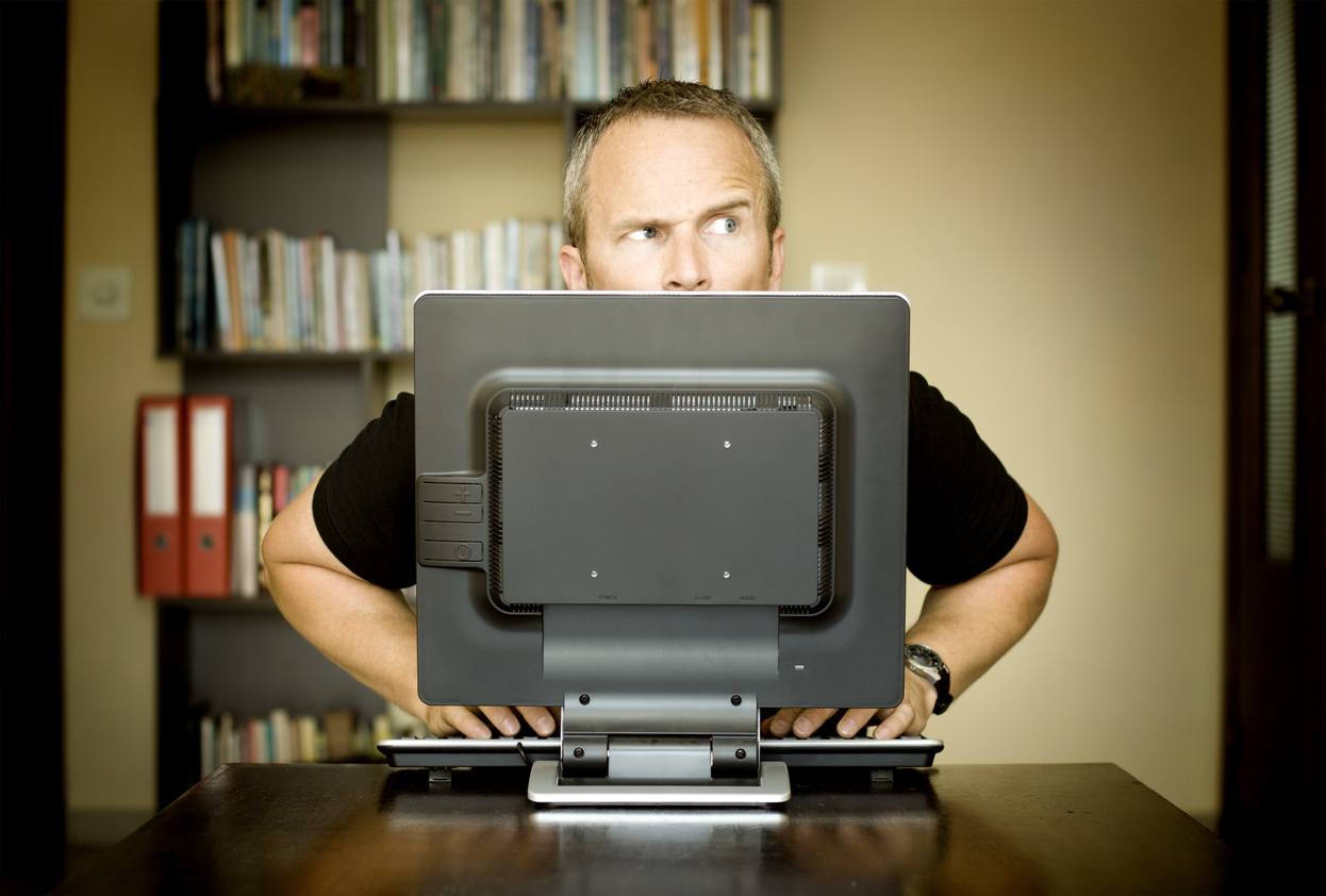 man sitting behind a desktop computer with a paranoid look on his face