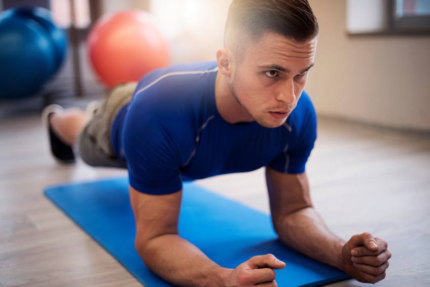 Young man holding a plank on a blue fitness mat