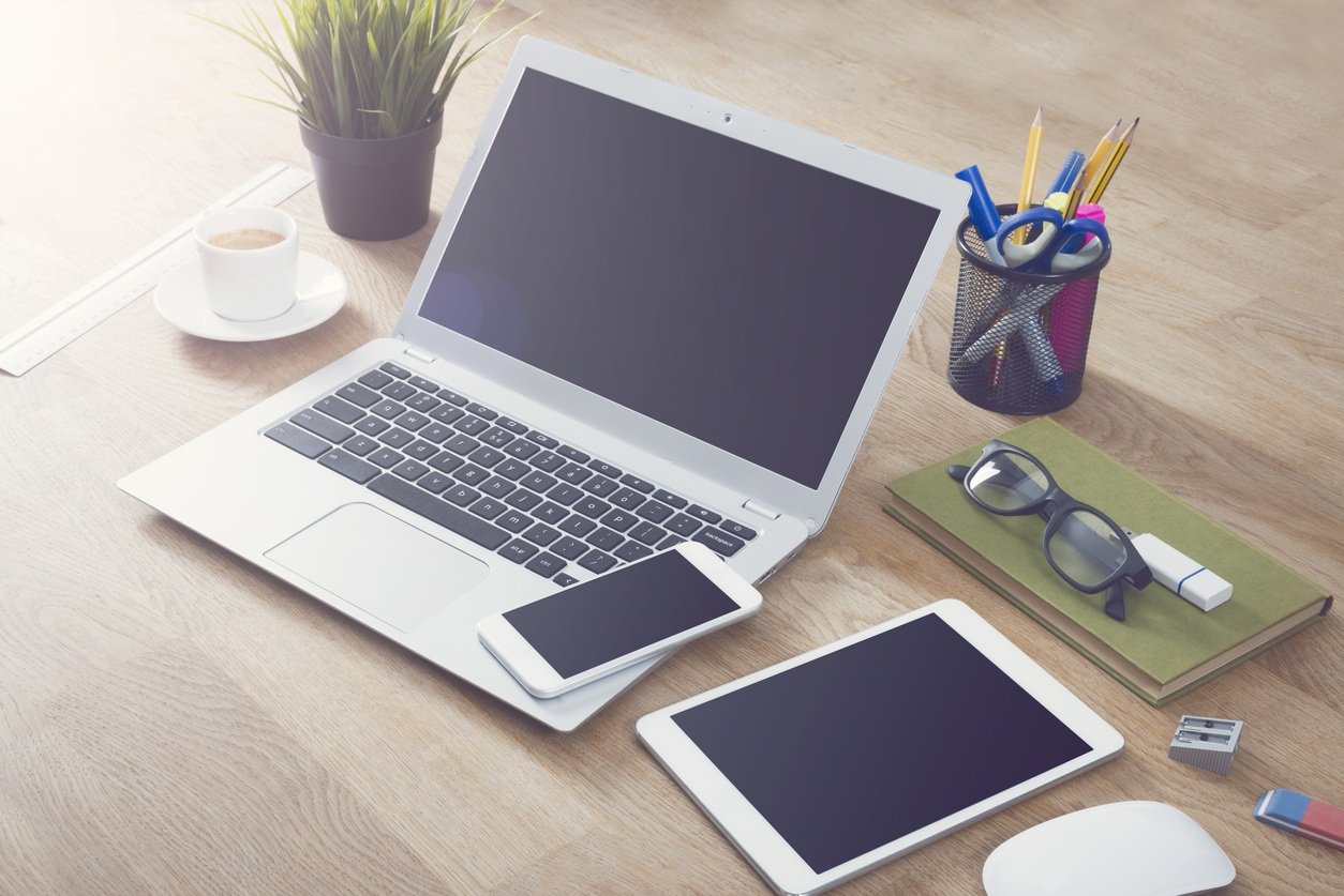 Laptop, smartphone, tablet with other desk items and coffee on table