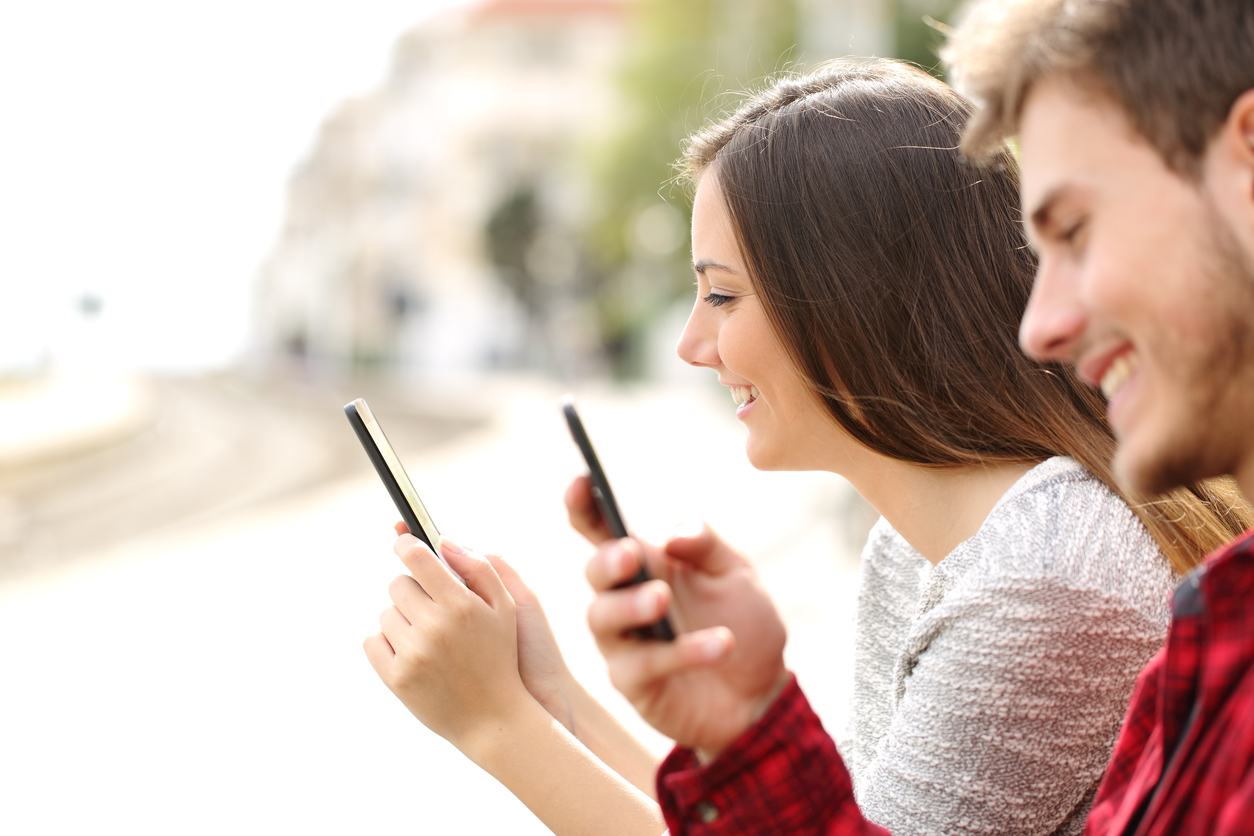 teen couple using smartphones in a train station