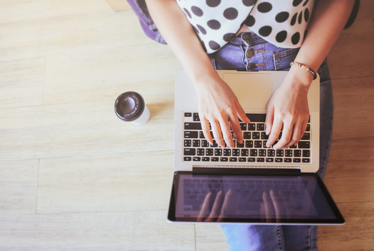 laptop in girl's hands sitting on wooden floor with coffee