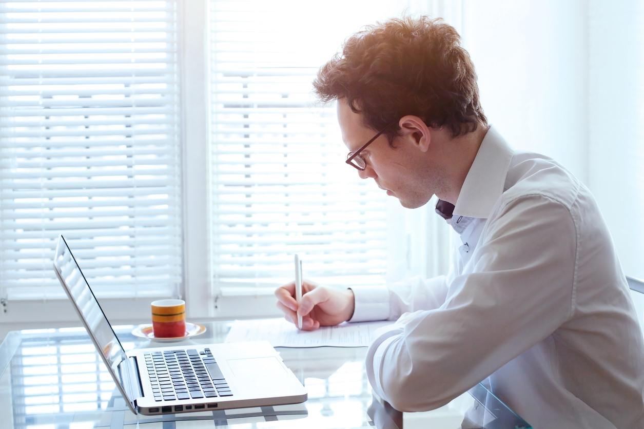man writing with laptop