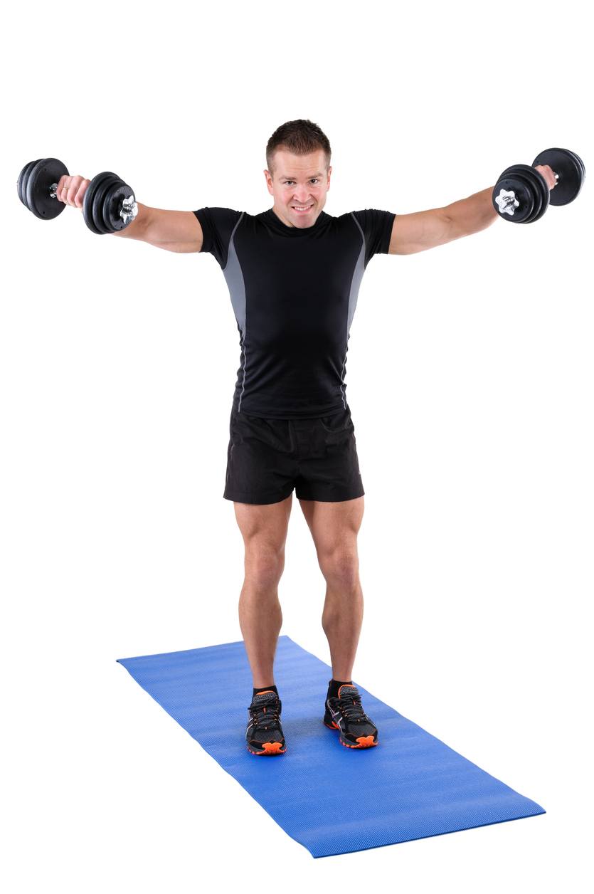 An instructor shows the finishing position of a standing dumbbell lateral raise