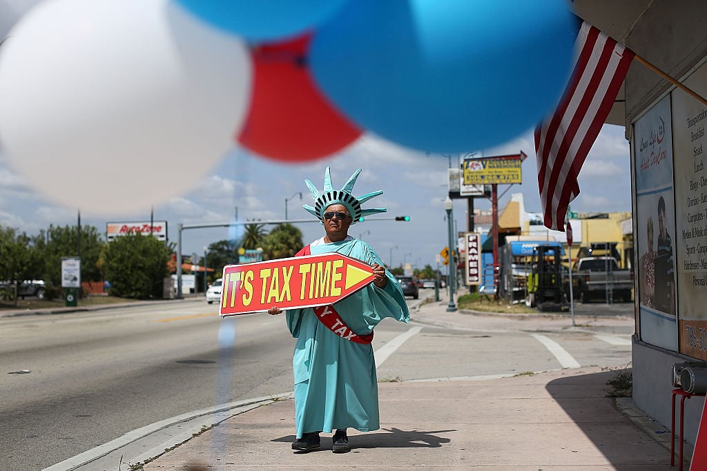 person dressed as Statue of Liberty waving sign that says "it's tax time"