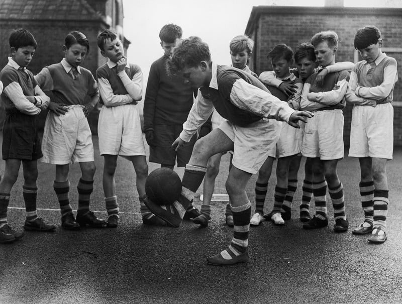 A young stand out demonstrates his ball skills to team-mates during after-school football practice in 1950s England