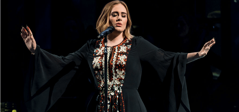 Adele has her eyes closed and her arms stretched out as she's singing on stage.