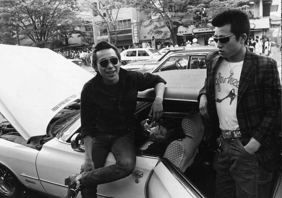 Teenagers hanging out next to a car