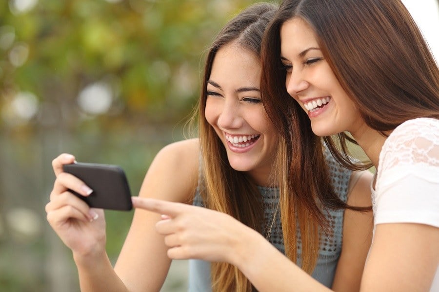 Two women friends laughing and sharing social media videos