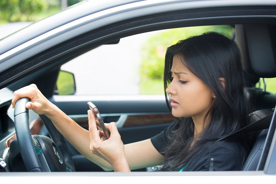 young woman driving in black car and checking her phone
