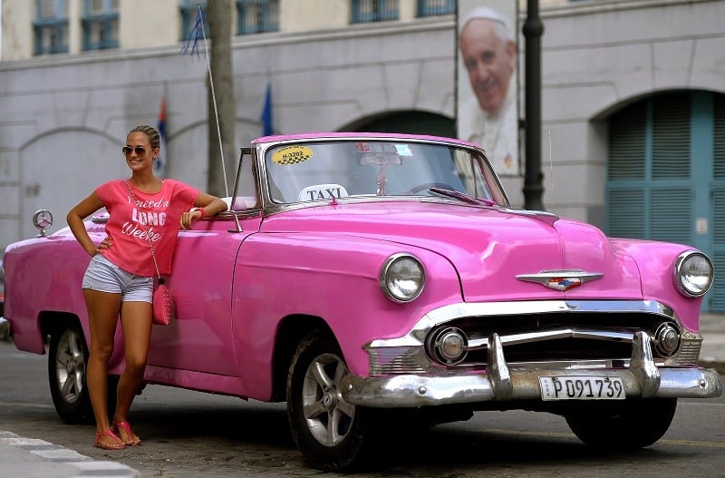A tourist leans by a taxi in front of a portrait of Pope Francis marking his visit to Cuba, in a street of Havana on September 17, 2015. The pope is visiting Cuba from September 19 to 22, the first stop on a trip that also will take him to the United States. In Cuba, he will visit Havana, the northeastern city of Holguin and Santiago de Cuba on the southeastern end of the island.