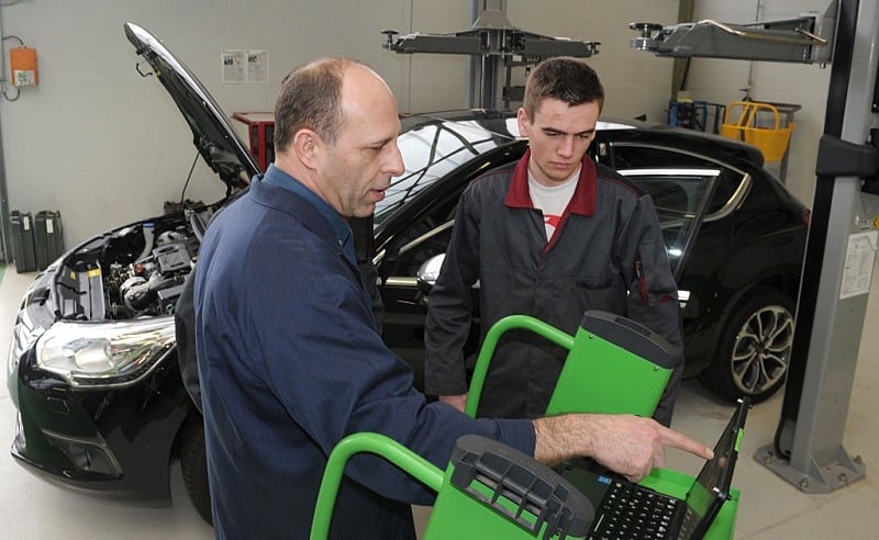 An apprentice mechanic works on a car with his trainer (L) at the Apprentice Training Center (CFA) of the Campus des Metiers (Job Campus) in Quimper, western France, on February 24, 2016.