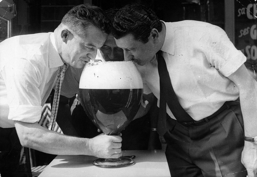 Three men drinking from a large glass of beer