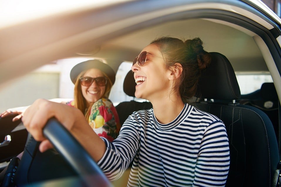 Smiling happy young woman giving her friend a lift in her car