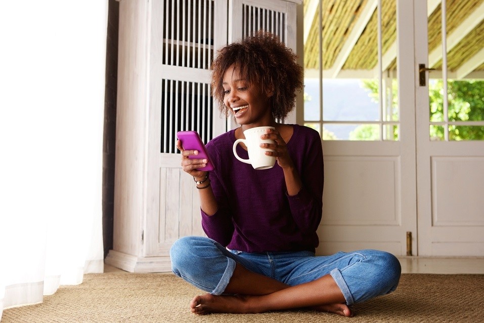 young black woman sitting on floor at home with smartphone