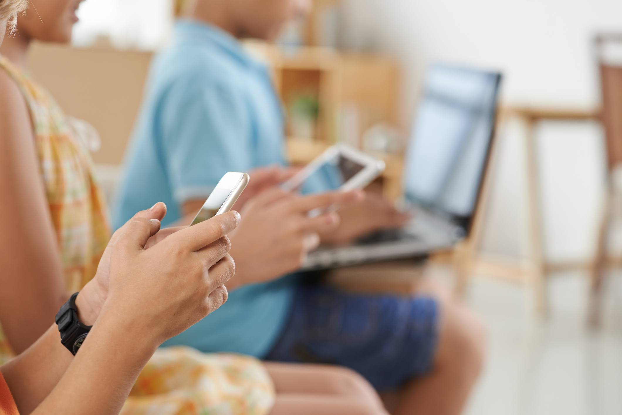 boy using smartphone while his friend is working on a laptop