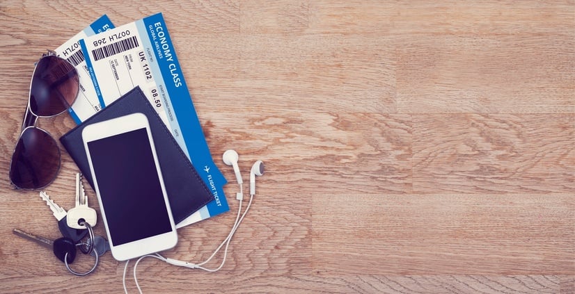 Airplane tickets, sunglasses, keys, and a cellphone and passport are laid out on a flat wooden surface