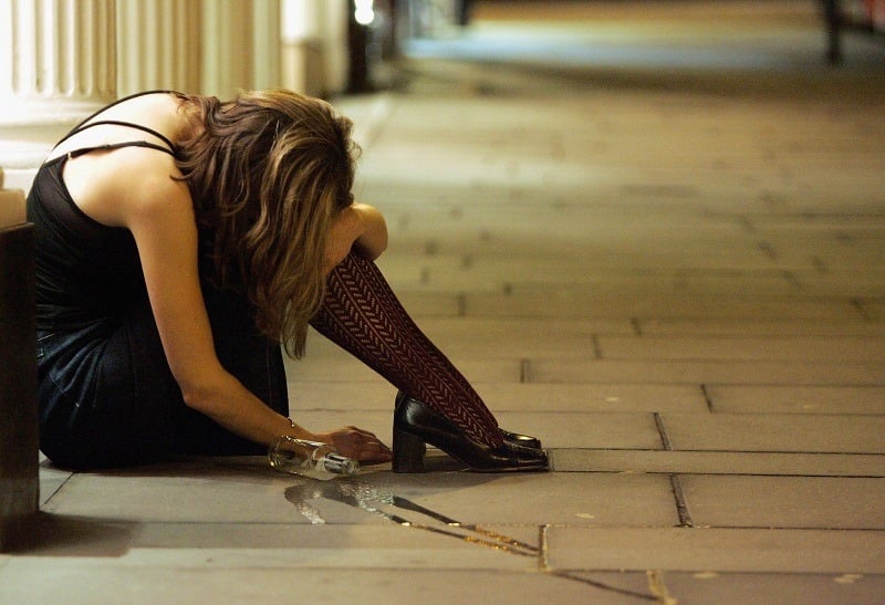 A woman, possibly fighting addiction, slumped over in front of a club