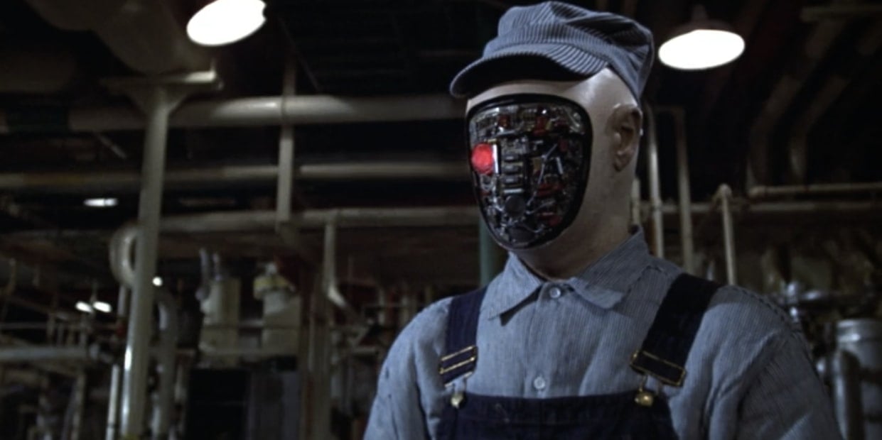 A robot with an exposed mechanical face stands in a warehouse. 