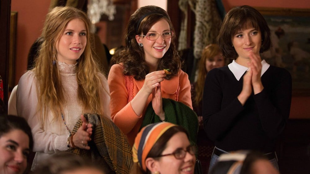 A group of women sit on a podium and clap in their hands in Amazon's Good Girls Revolt