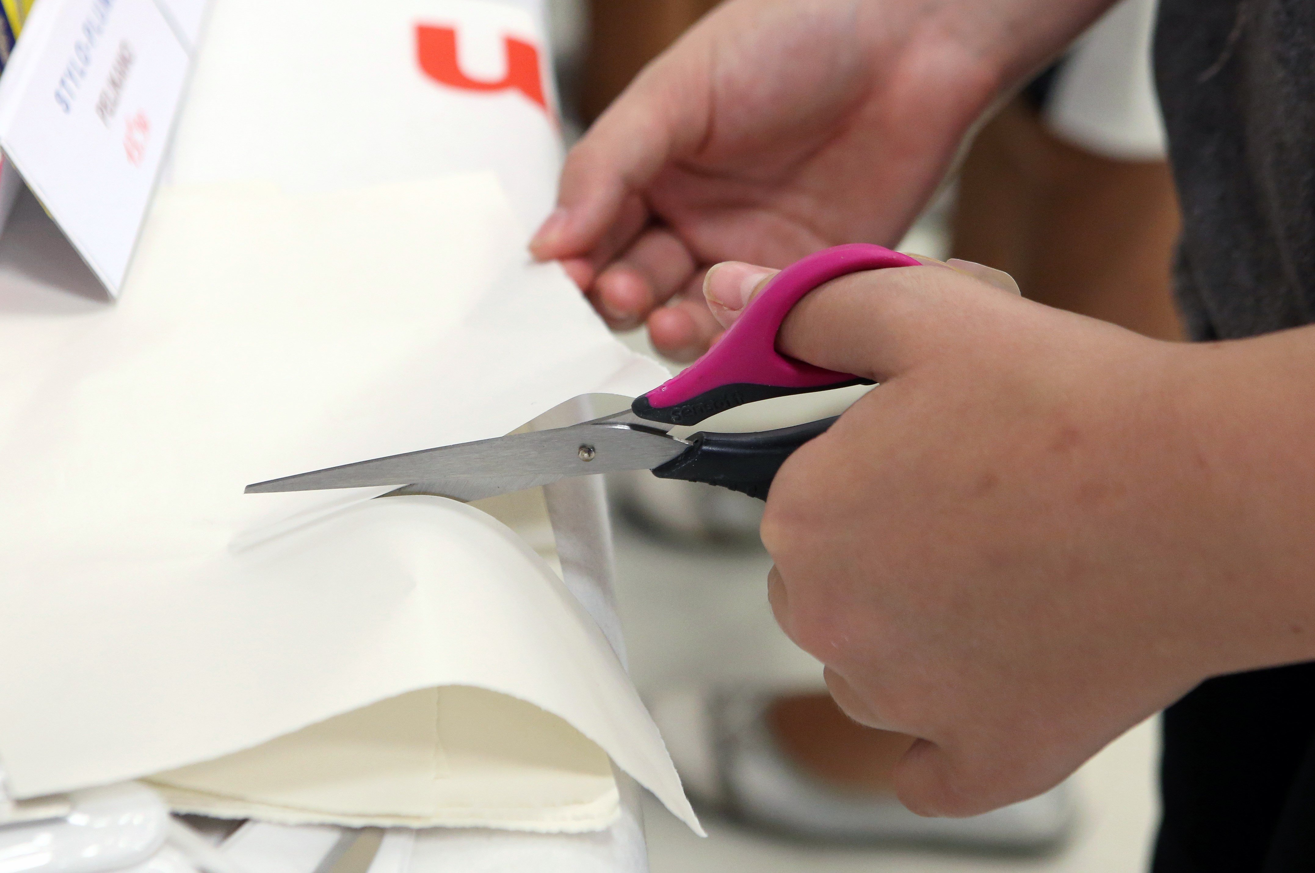 A person cuts paper with scissors for left-handed users