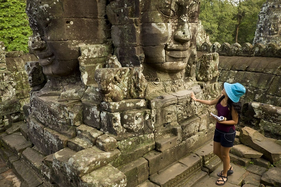 young visitor meets giant stone heads at the top terrace of the Bayon, at Angkor Thom, Cambodia