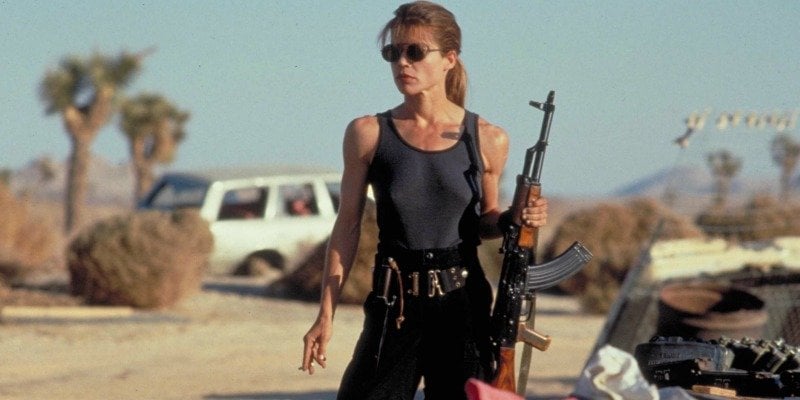Woman in a tank top and sunglasses holding a rifle in the desert