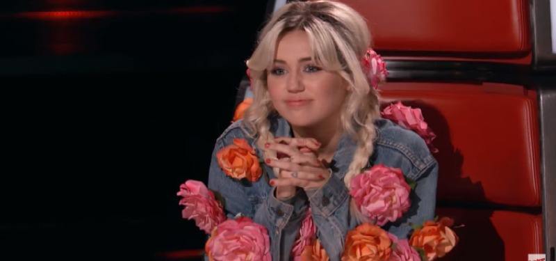 Miley Cyrus is wearing a denim jacket with flowers on it on The Voice.