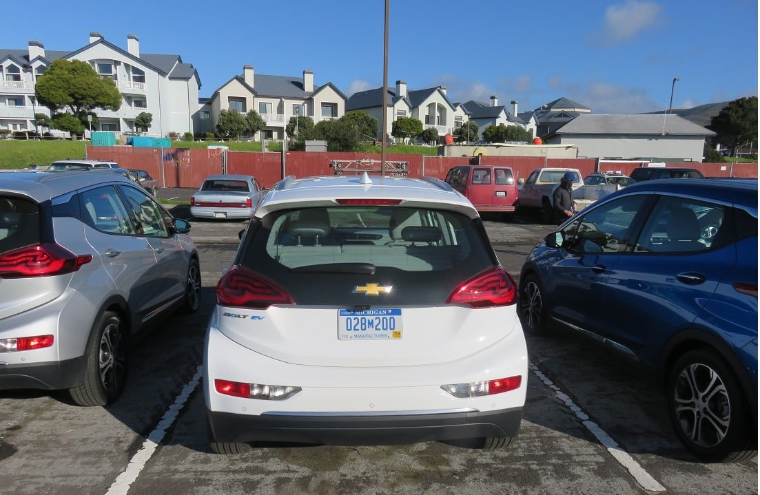 A white 2017 Chevrolet Bolt EV sits parked in a lot across from a residential area