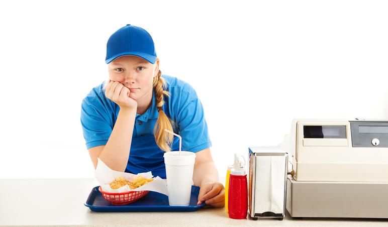 Teenage worker in a fast food restaurant bored and leaning on the counter