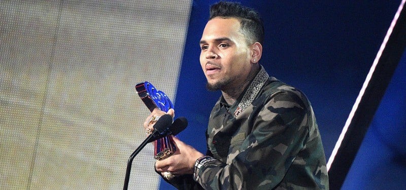 Chris Brown speaking into a microphone, wearing a black leather jacket