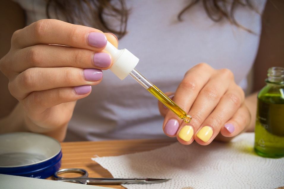 A young girl sits at a table and gets a yellow oil on the nails