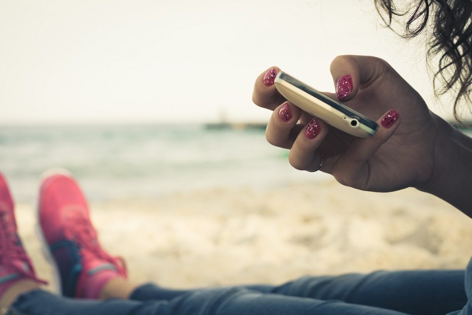 Girl on the beach and using a mobile phone to write Instagram captions