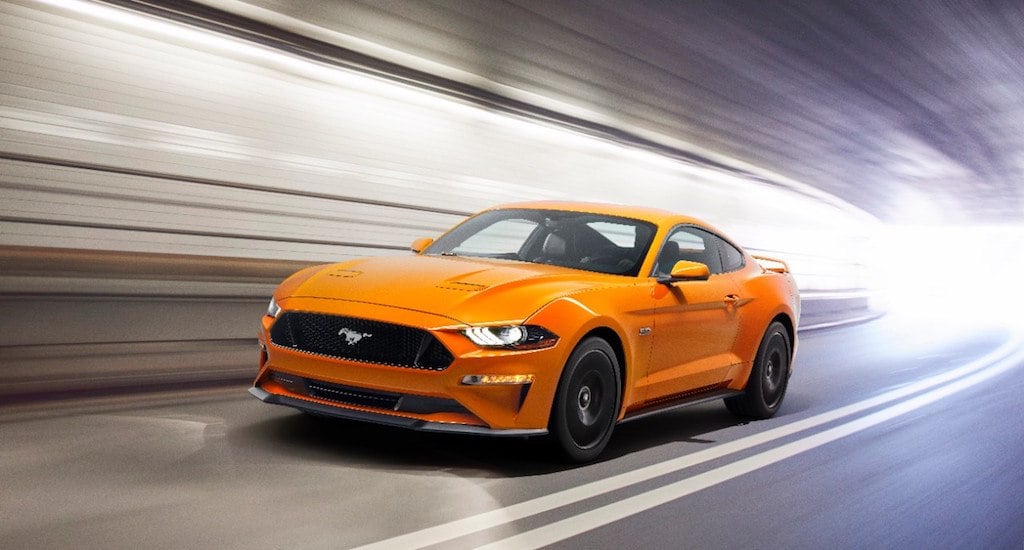 A bright orange 2018 Ford Mustang GT accelerates through a tunnel