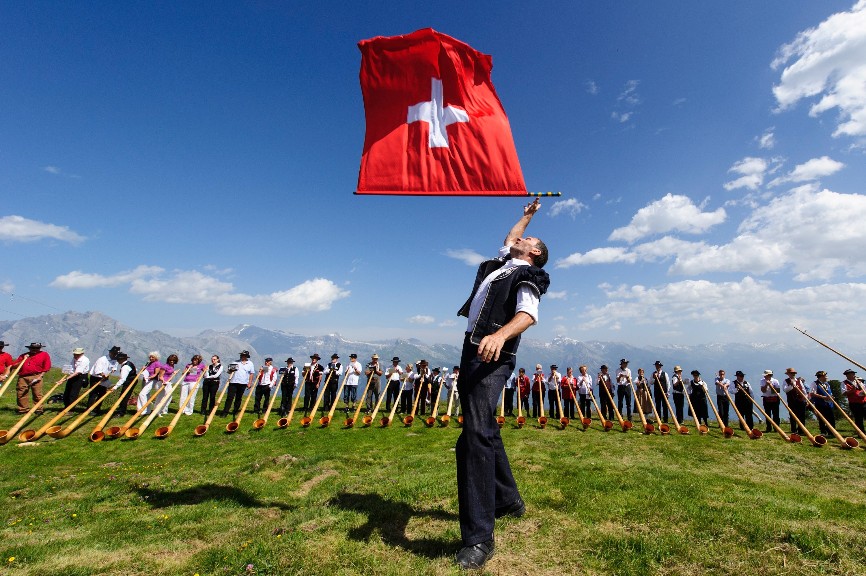 A man throws a Swiss flag as alphorn players perform